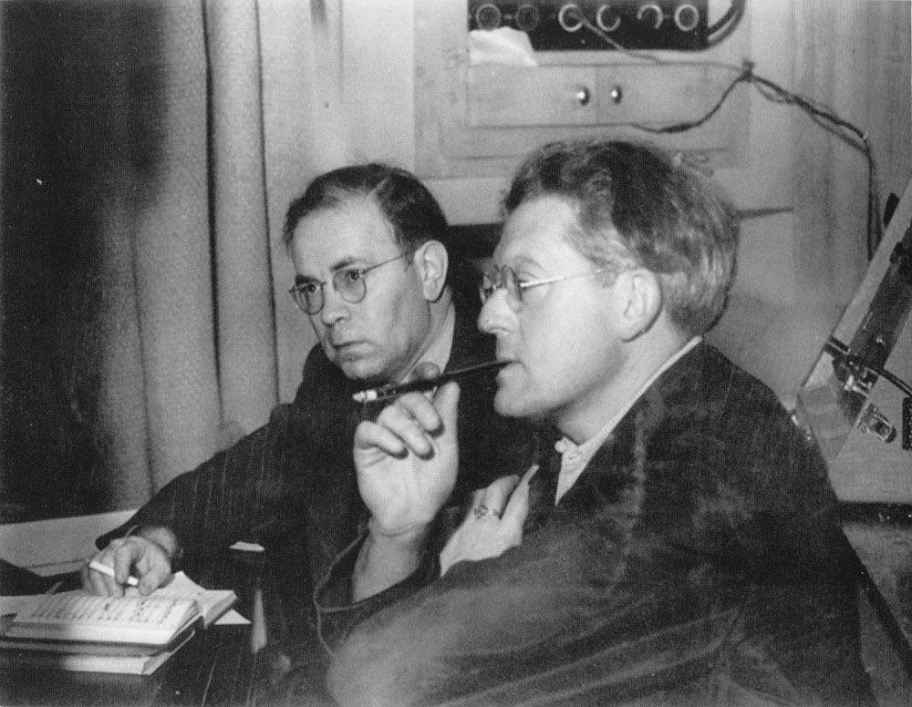 Rodzinski is seated and holding a cigarette holder in his mouth while he contemplates the playback of a prospective recording by The Cleveland Orchestra. A small score is open in front of him. 