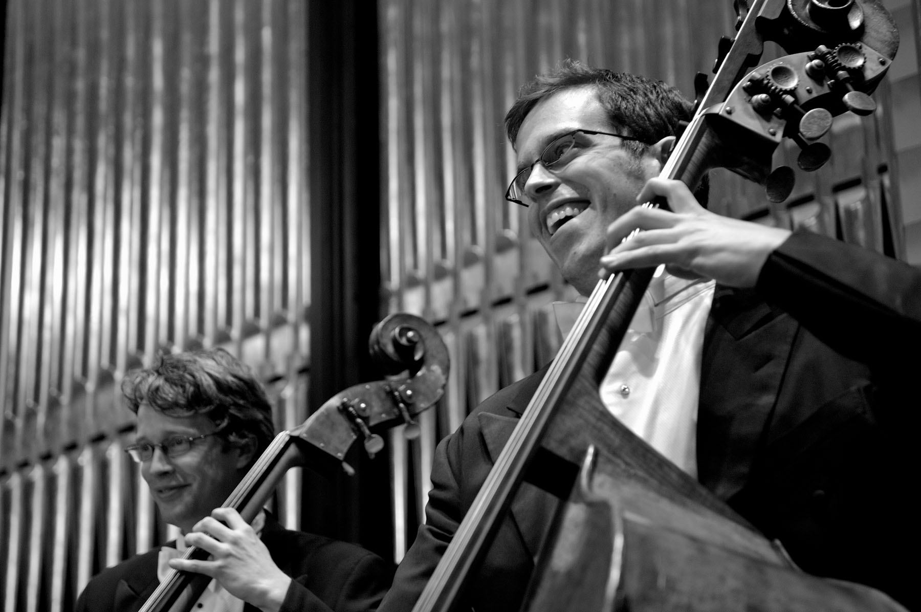 Two musicians playing the bass and smiling broadly.