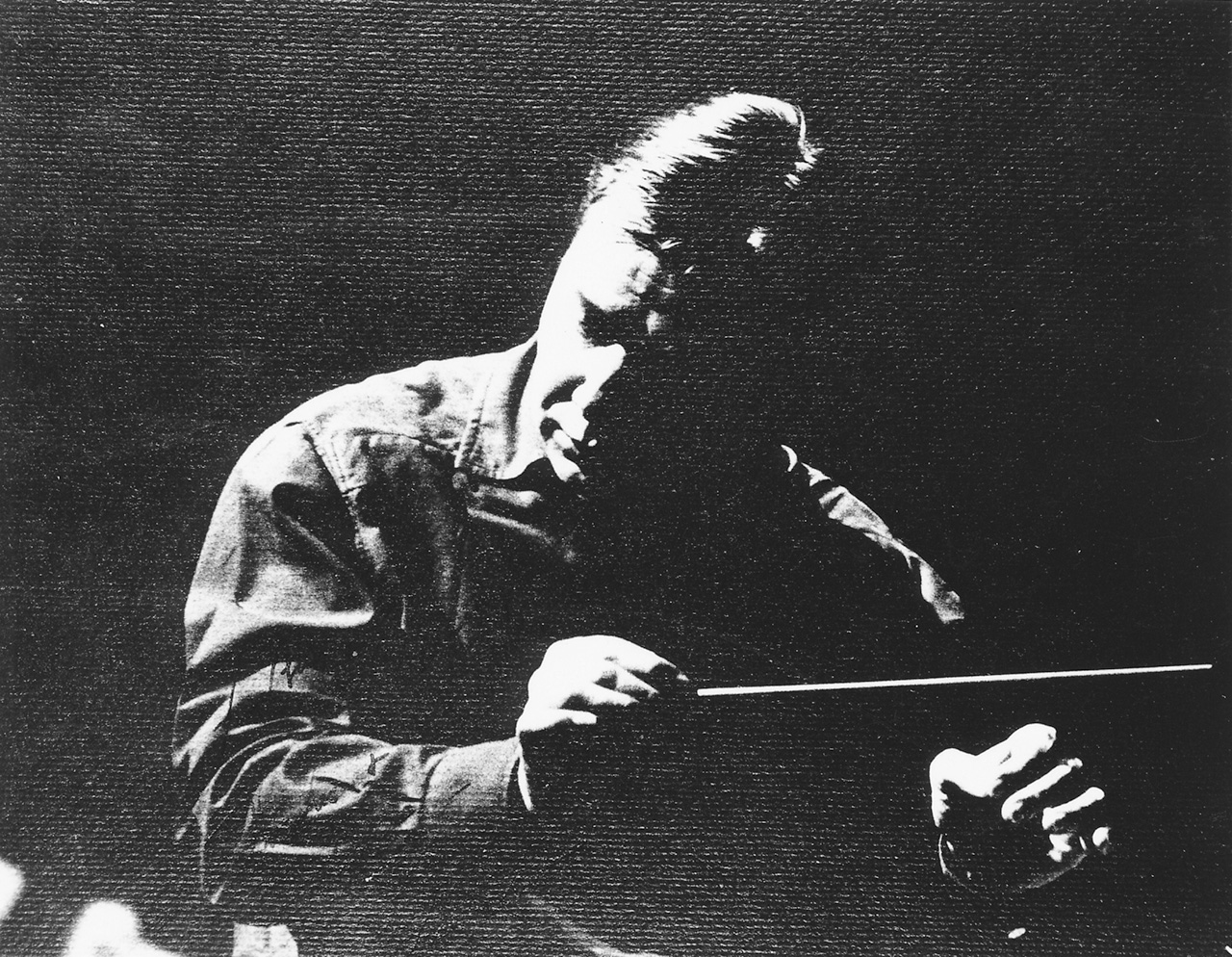 A man in shadow, conducting with a baton.